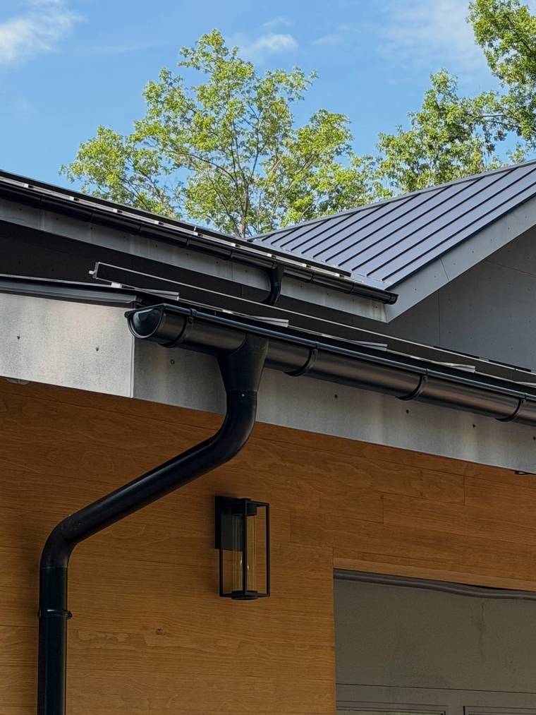 Black seamless gutter and downspout on a standing-seam metal roof, installed by WB Construction